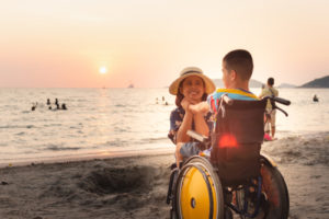 A child with Cerebral palsy on a beach with their parent