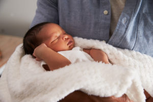 baby sleeping in blanket in parent’s arms