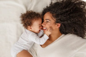 mother and baby lie on bed and smile at each other