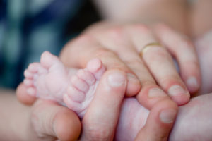 man gently holding baby’s feet in both hands
