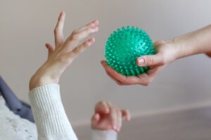 The hands of a child with cerebral palsy exercises with a ball. Learn the cost to file a cerebral palsy lawsuit.