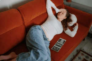 A pregnant woman lies down on the couch after experiencing severe nausea. She called her doctor to ask what hyperemesis gravidarum is.